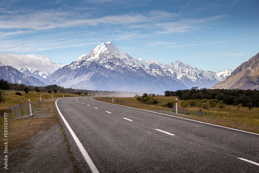 Fototapeta premium a long road surrounded by green trees and tall mountains near water