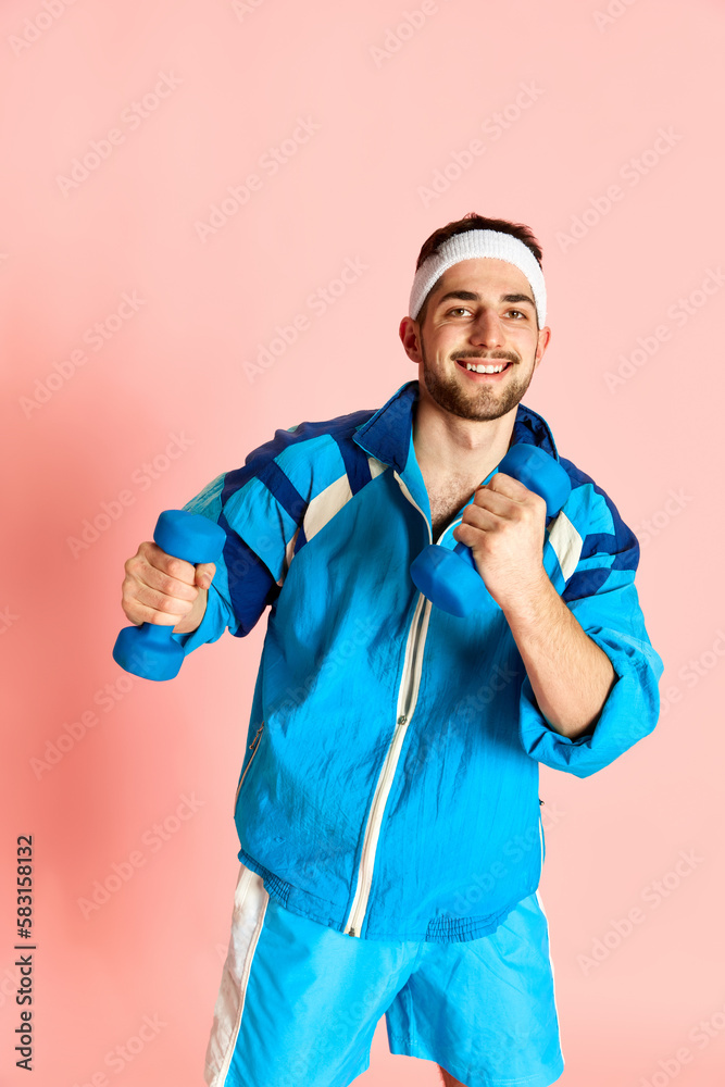 Portrait of young active sportive man in blue sportswear training, posing with dumbbells against pink studio background. Concept of sportive lifestyle, emotions, facial expression. Ad Portrait of young active sportive man in blue sportswear training, posing with dumbbells against pink studio background. Concept of sportive lifestyle, emotions, facial expression. Ad