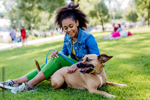 Multiracial girl sitting and resting with her dog outside in the park, training him, spending leisure time together. Concept of relationship between dog and teenager, everyday life with pet.