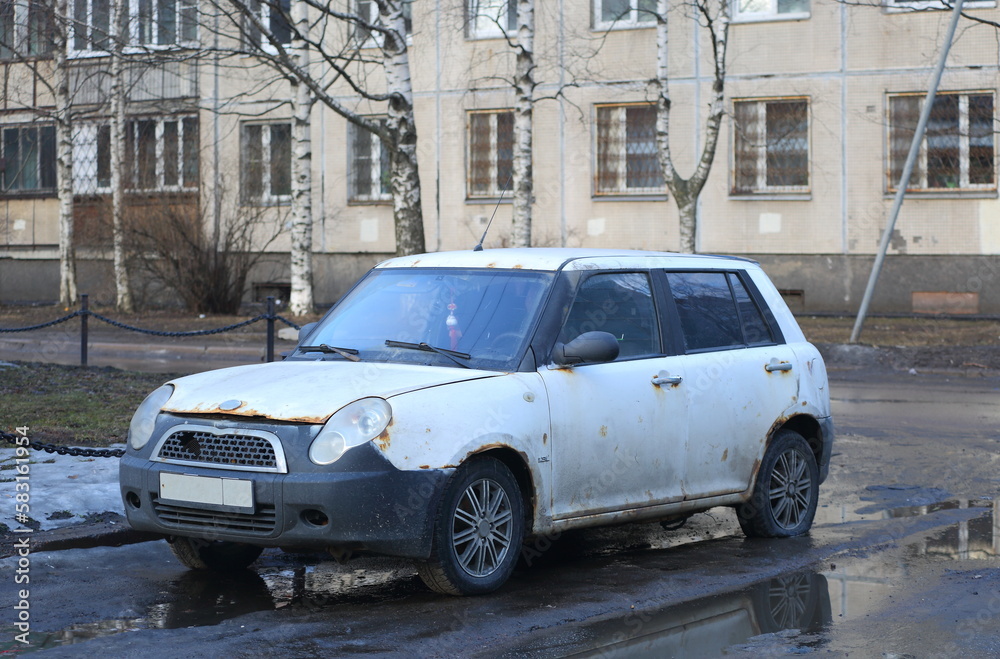 An old white rusty car is parked on the city street, Iskrovsky Prospekt, St. Petersburg, Russia, March 2023