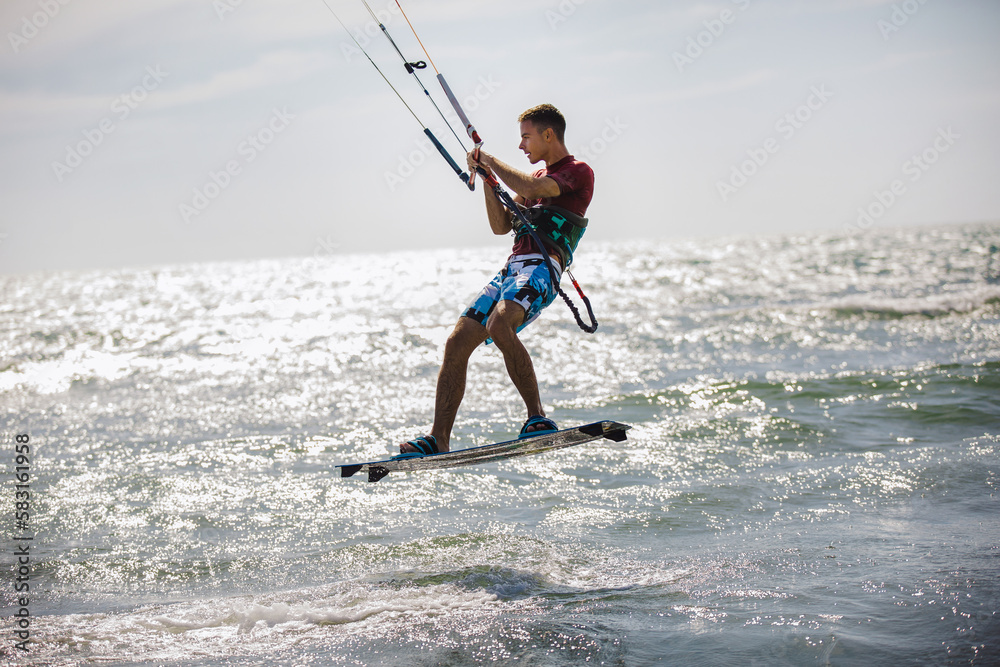 Naklejka premium Professional kiter does the difficult trick. A male kiter rides against a beautiful background of waves and performs all sorts of maneuvers.