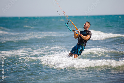 Professional kiter does the difficult trick. A male kiter rides against a beautiful background of waves and performs all sorts of maneuvers.