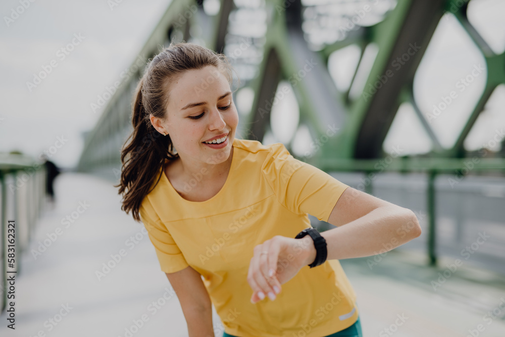 Young woman checking smartwatch in city, preparing for run, healthy lifestyle and sport concept.