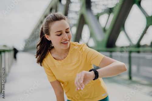 Fototapeta Naklejka Na Ścianę i Meble -  Young woman checking smartwatch in city, preparing for run, healthy lifestyle and sport concept.