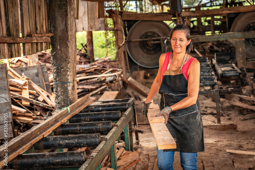 Woman smiles and winks one eye looking at camera, loading a board in a sawmill.