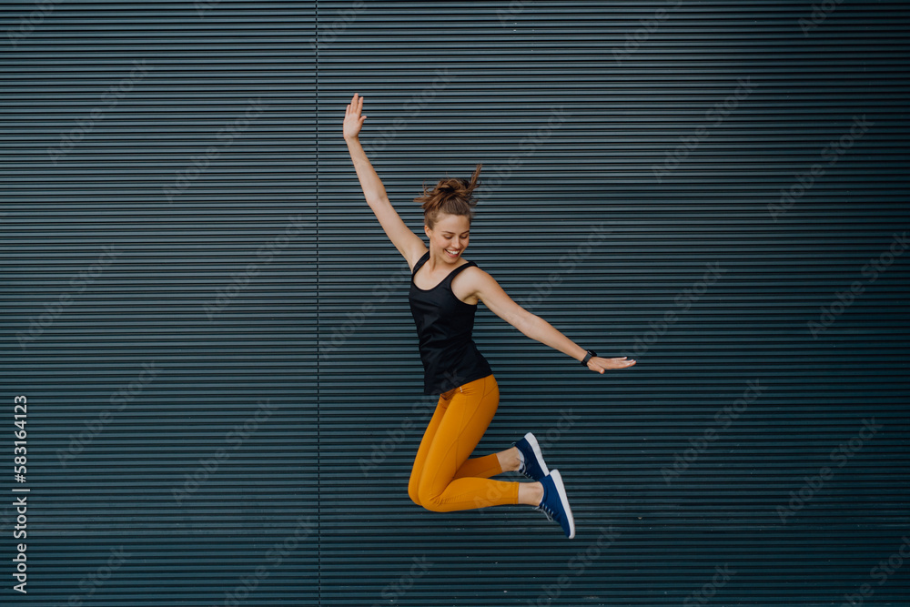 Portrait of young excited woman jumping outdoor in city.
