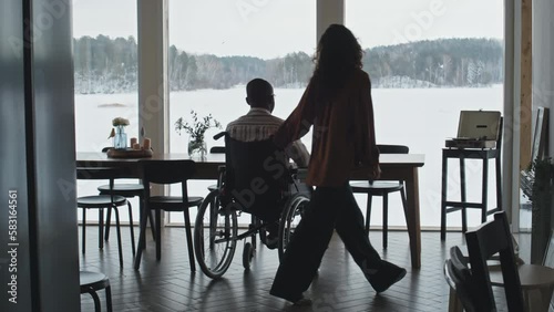 Wallpaper Mural Caucasian woman driving black man in wheelchair to living room with panoramic window overlooking rural winter landscape and sitting down at table in front of him with friendly smile Torontodigital.ca