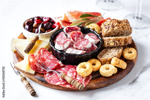 Meat and cheese platter with bread slices, typical Spanish tapas with serrano ham, fuet sausage, salami, goat chees, spicy olives and fresh bread and wine