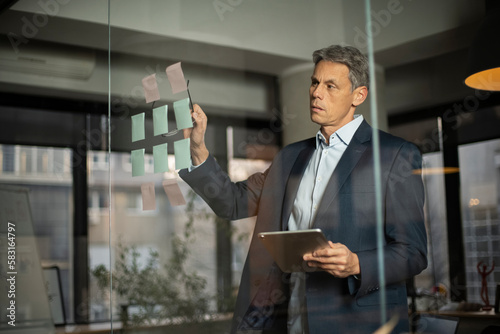 Portrait of successful businessman in office. Man writing ideas on colorful stickers on glass wall.