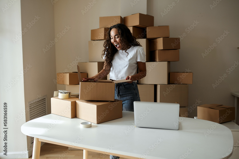 Smiling satisfied young woman, packs a package, opens a parcel, happy consumer girl holds a cardboard box, receives a good purchase in an online store at home, collects mail. mail delivery concept