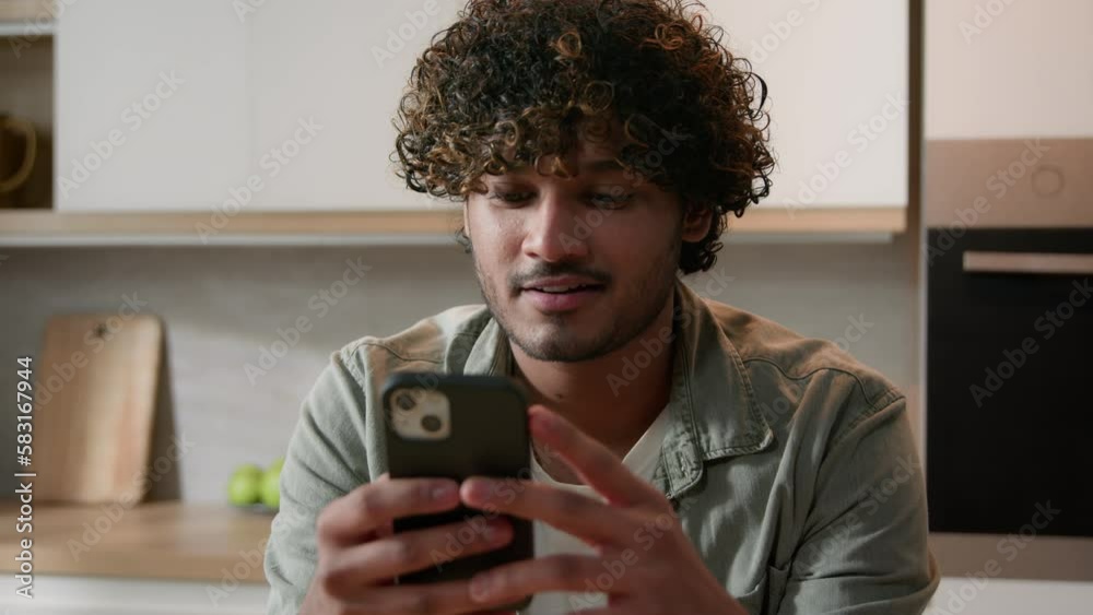 Carefree Indian man using smartphone laugh Arabian male smiling phone shopping app social media joke fun reading news watching video online laughing funny mobile technology chatting smile at kitchen