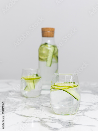 Bottle with two glasses of beauty water lemonade made of cucumber and lime standing on the white marble table