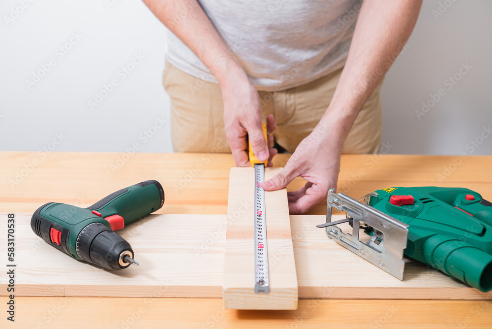 A man works with a jigsaw and a screwdriver on a wooden table with and without gloves, also measures with a tape measure A man works with a jigsaw and a screwdriver on a wooden table with and without gloves, also measures with a tape measure