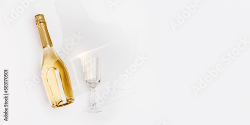 Top view white sparkling wine bottle and glass wine with sun shadow and glare on light white background. Flat lay golden champagne bottle. Summer alcoholic drink concept, banner with copyspace, above