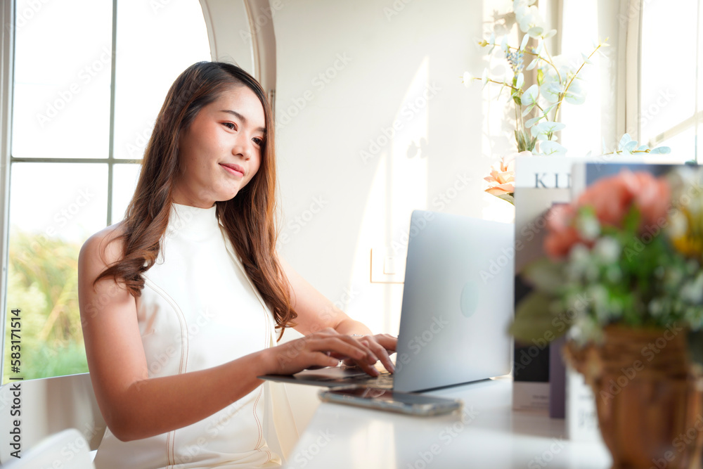 Fototapeta premium Asian woman with curly hair is working chatting with clients or colleagues via communication channels, telephone, internet with her laptop and mobile phone.
