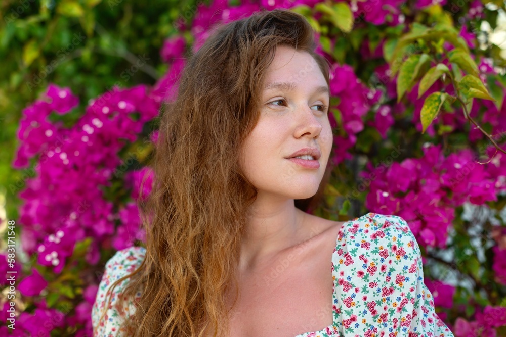 Fototapeta premium Portrait of happy beautiful girl, young positive woman is smelling beautiful pink flowers in the garden, smiling, enjoying spring or summer day, breathing deep deeply fresh air