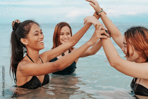 Three happy asian women play wrestling while taking a dip at the beach and having fun. A fun vacation during the summer.