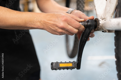 detail of a woman's hands fixing the pedal of a bicycle, bicycle workshop for the personal maintenance of a means of transportation.