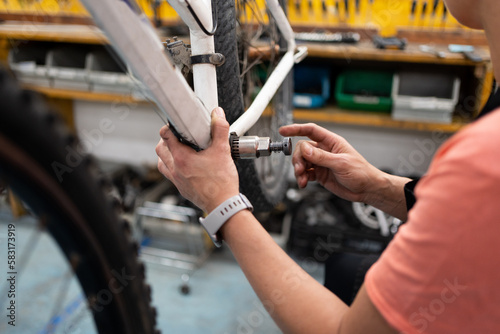 Detail of woman's hand removing nut from bike pedal space, workshop with bike hanging and female mechanic working on maintenance, wrist with smart watch