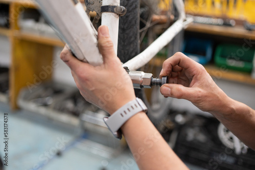 Detail of woman's hand removing nut from bike pedal space, workshop with bike hanging and female mechanic working on maintenance, wrist with smart watch