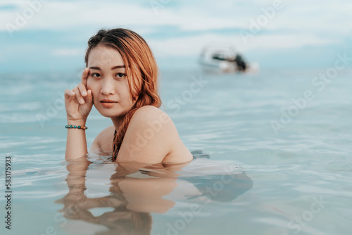 A young pensive asian woman taking a dip at the beach. A female tourist unwinding in chest deep waters. Vacation scene.