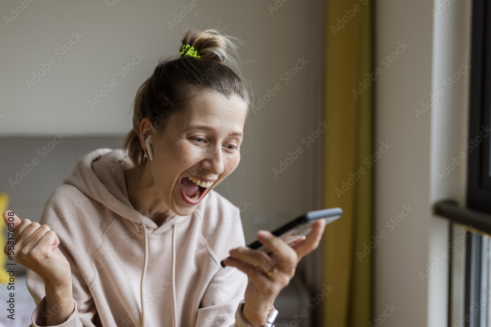 Young caucasian woman using mobile phone and wireless headphones, resting, sitting on bed at home and listening podcast or clubhouse - voice-only social media app, drop-in audio chat Young caucasian woman using mobile phone and wireless headphones, resting, sitting on bed at home and listening podcast or clubhouse - voice-only social media app, drop-in audio chat