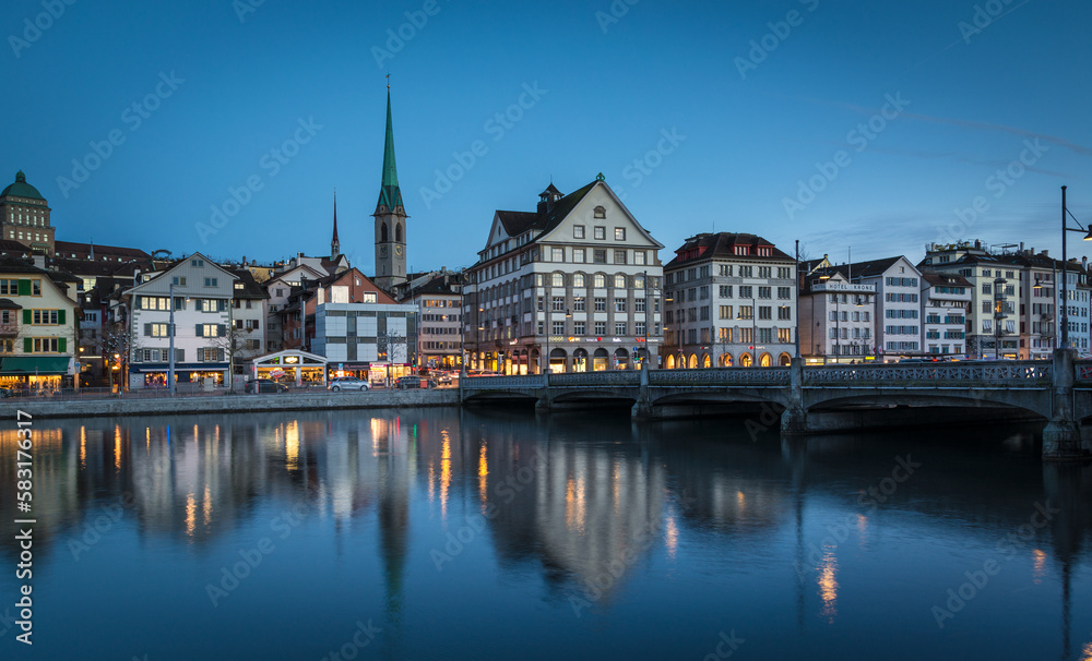 Panorama of Zürich city center with historical buildings and church at water with bridge during evening