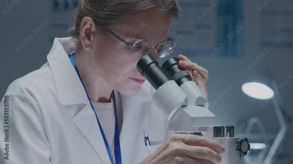 Experienced female lab worker looking in microscope when conducting research in clinical laboratory. Medium close-up shot Experienced female lab worker looking in microscope when conducting research in clinical laboratory. Medium close-up shot