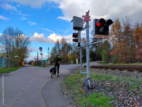 A cyclist is waiting at railway crossing with stoplights being turned on. The weather is sunny.