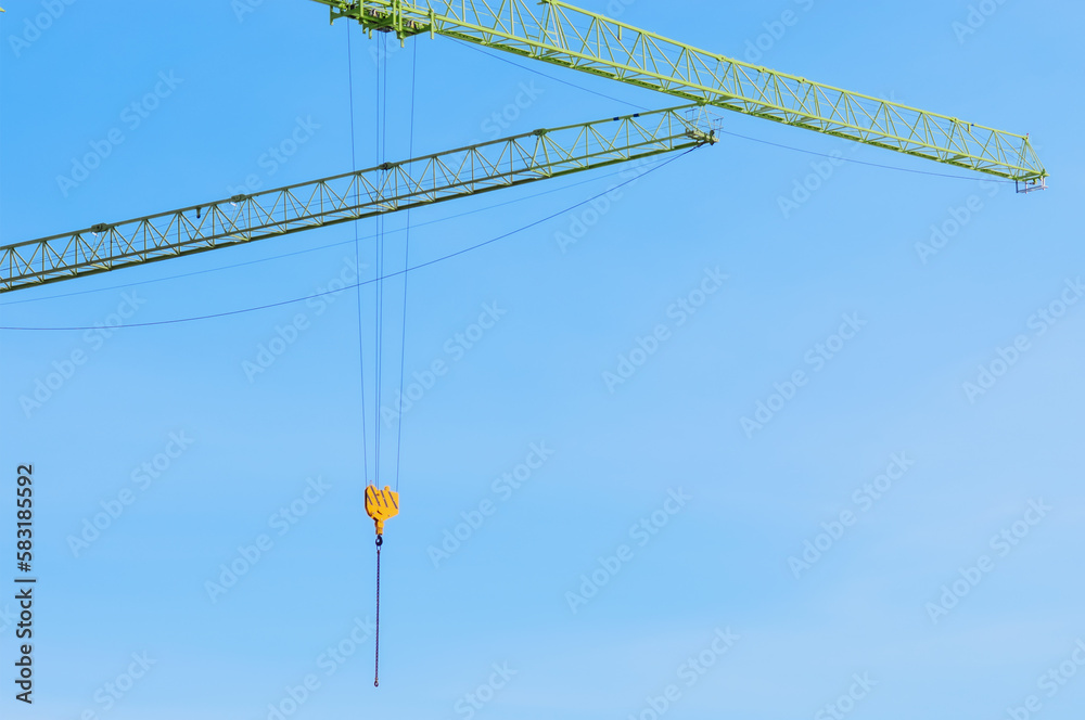 Two jib cranes against the blue sky. Large construction equipment. Ropes, metal structures and hook lifting device. Construction industry concept with copy space for text. No people Two jib cranes against the blue sky. Large construction equipment. Ropes, metal structures and hook lifting device. Construction industry concept with copy space for text. No people