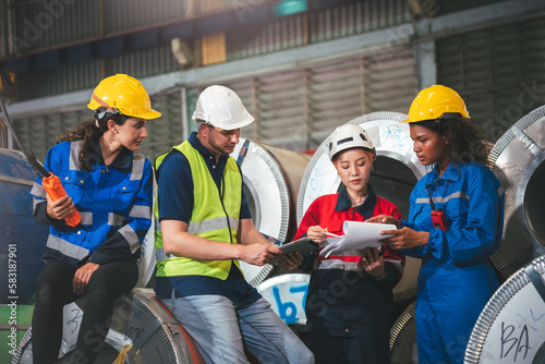 Group of diverse warehouse worker in safety suit, Project manager using blueprint and digital tablet to discussing with engineer team for work in construction industry. Teamwork and unity concept.