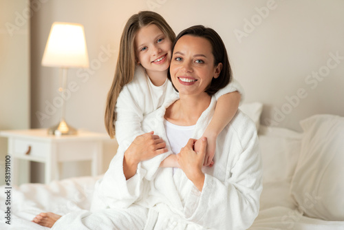 Love, relationship mom and daughter at home. Smiling caucasian small girl hugging young woman in bathrobe