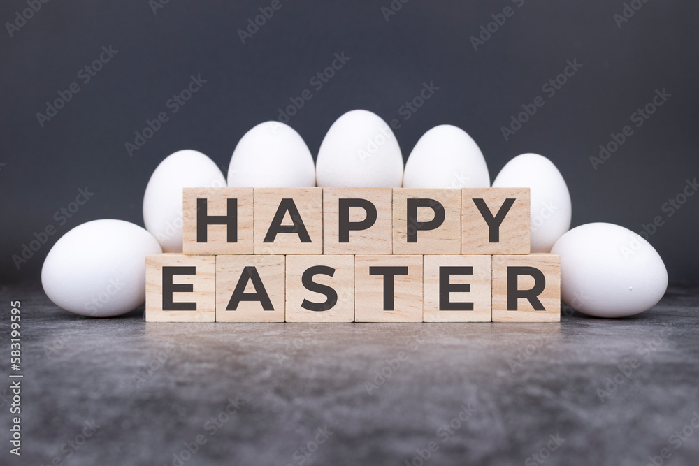 Happy Easter on wooden cubes, in front of white eggs standing and lying on a stone background. Modern design.