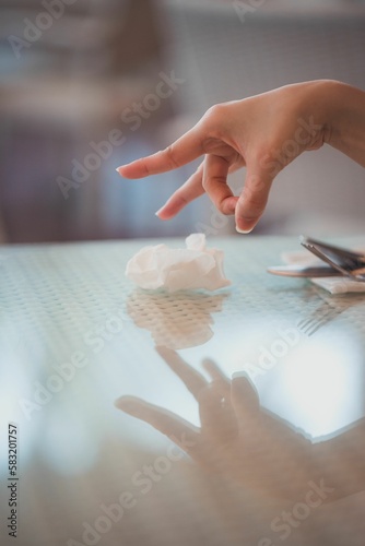 Female hand in a flicking pose, preparing to flick the tissue off the glass table with reflection