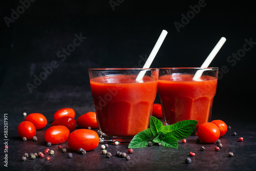 Fresh tomato juice in a glass with tomatoes, pepper on a dark background