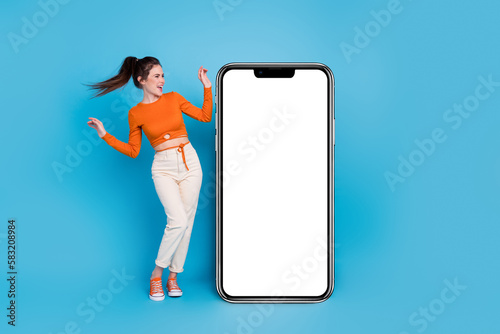 Full length photo of impressed millennial brunette lady look poster wear top pants sneakers isolated on blue background