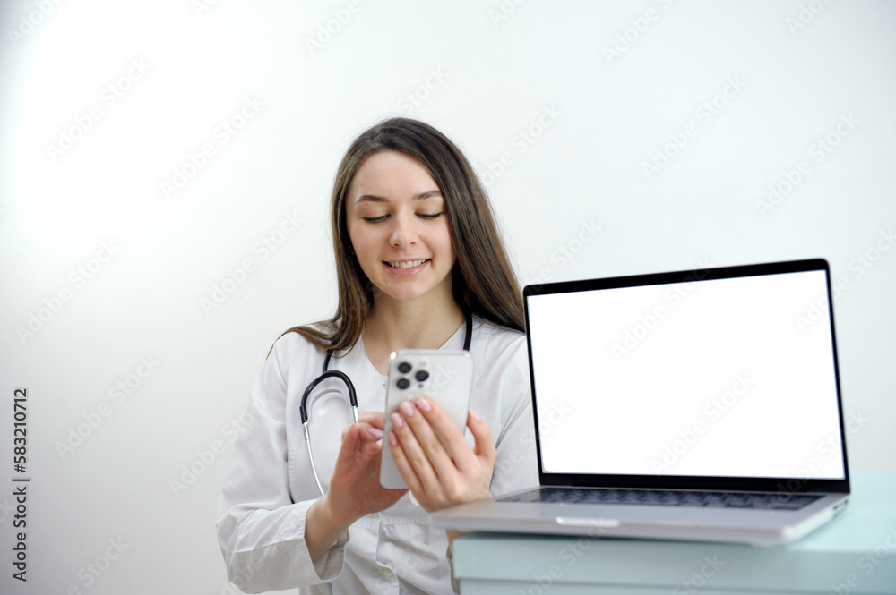 friendly female doctor over white background with a laptop. woman doctor working on the phone answering the call in front of her laptop with white screen space for advertising High quality photo - obrazy, fototapety, plakaty 