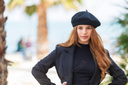 a stunning look of a beautiful young girl with long curly red hair wearing a beret and black shirt and textured background of the sea and palm trees © Antonio Conte