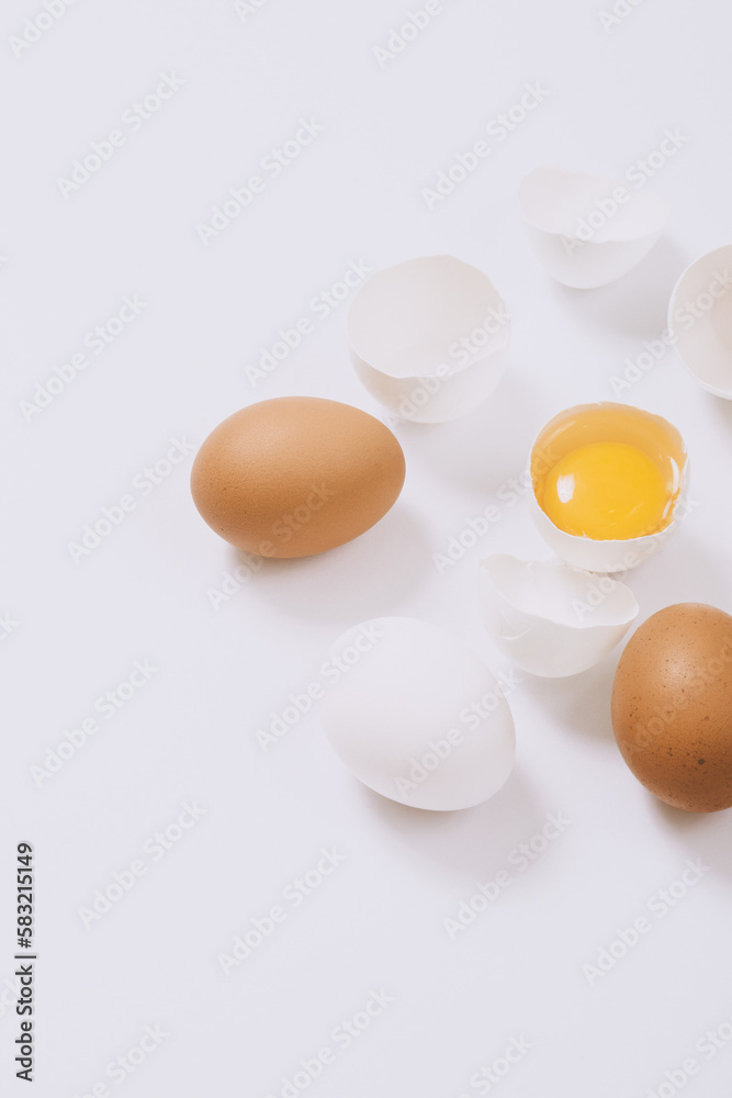 Whole white and brown eggs and cracked egg half with a yolk on bright background. Selective focus. Whole white and brown eggs and cracked egg half with a yolk on bright background. Selective focus.