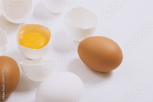Whole white and brown eggs and cracked egg half with a yolk on bright background. Selective focus.