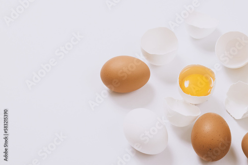 Whole white and brown eggs and cracked egg half with a yolk on bright background. Selective focus.