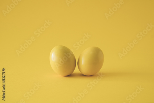 Two yellow colored eggs on yellow background. Minimal Easter concept.