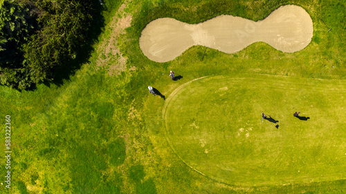 Aerial view of a golf course with green hills and sand bunkers. There are golfers playing a hole in the sports club. Sports concept.