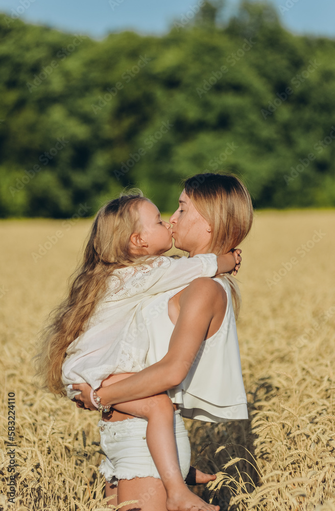 Growing wheat. Food security. A woman holds her little daughter in her arms and stands in a wheat field in summer. Growing wheat. Food security. A woman holds her little daughter in her arms and stands in a wheat field in summer.
