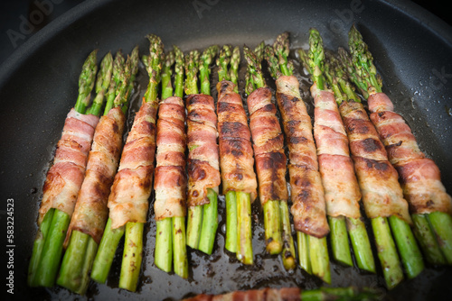 Viele Bündel grüner Spargel im Speckmantel in der Pfanne