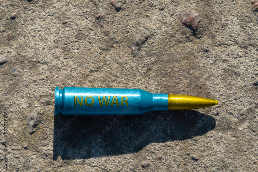 A yellow-blue rifle cartridge with the inscription NO WAR lies on a concrete surface (close-up). The concept of military support for Ukraine A yellow-blue rifle cartridge with the inscription NO WAR lies on a concrete surface (close-up). The concept of military support for Ukraine