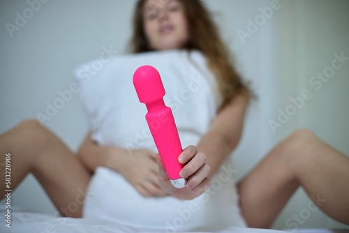 Young happy sexy woman hold in hand sex toy, masturbate with vibrator in bed in bedroom at home. photo