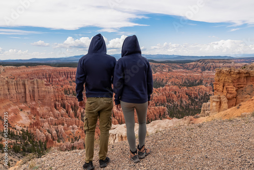 Rear view of loving couple in hoodies with aerial view of massive hoodoo sandstone rock formations in Bryce Canyon National Park, Utah, USA. Natural amphitheatre sculpted red rocks of Claron Formation