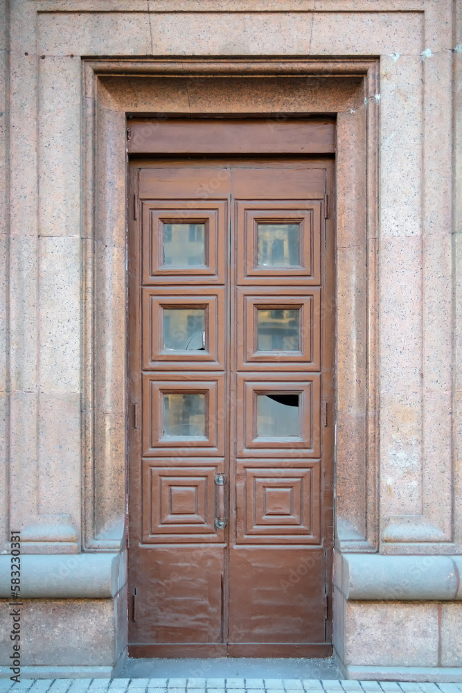 Tall old wooden door with square ornament and broken glass