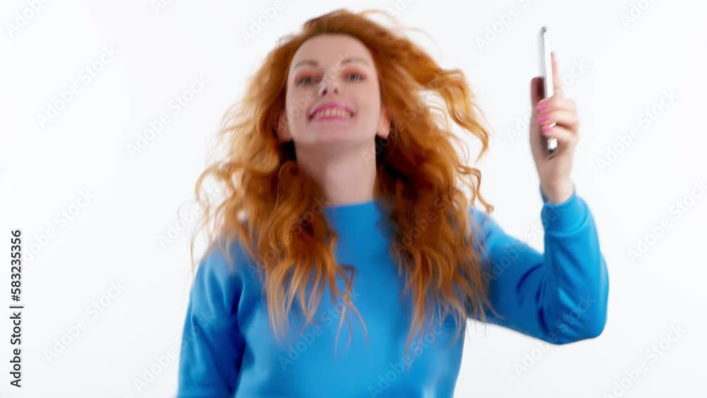 Smiling overjoyed woman nodding yes with smart phone, winner gesture, say Yes. Positive happy young 20s lady showing approving gesture with mobile phone in blue sweatshirt. Success concept Smiling overjoyed woman nodding yes with smart phone, winner gesture, say Yes. Positive happy young 20s lady showing approving gesture with mobile phone in blue sweatshirt. Success concept